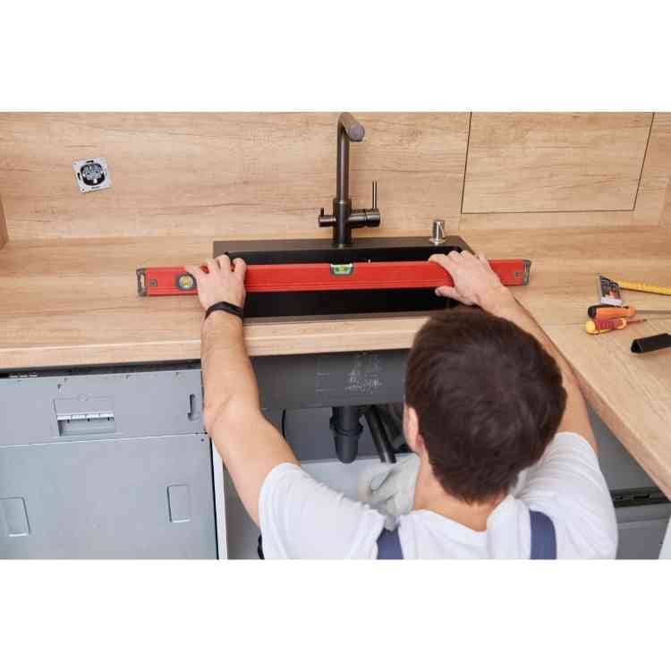 Plumber holding a level over a kitchen sink install to ensure it is installed level